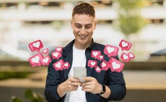 This image shows a young man smiling and using his smartphone in an urban environment. He is surrounded by animated heart icons, likely representing likes photo