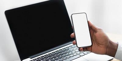 A hand holds a smartphone with a blank screen near a laptop with a black screen. photo