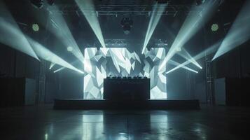 A stage with a DJ setup and a geometric patterned backdrop. The lights are on and the stage is ready for a performance. photo