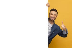 A man with a beard is standing and holding a sign in one hand while giving a thumbs up with the other hand. He appears to be expressing positivity or agreement. photo