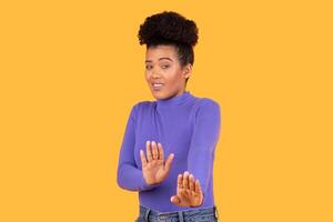 The young woman smiles and holds her hands up with a playful expression, standing in front of a vibrant yellow background. Her casual style adds to the lighthearted atmosphere of the moment. photo