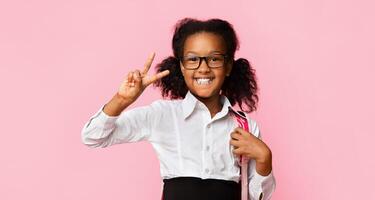 Victory. Cheerful Elementary School Girl Gesturing V-Sign Smiling To Camera Standing Over Yellow Studio Background. Panorama, Studio Shot photo