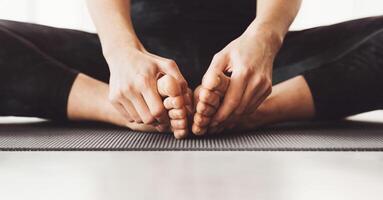 Cropped of woman is seated on a yoga mat in a cross-legged position, gently pulling their toes forward as part of a stretching routine, panorama photo