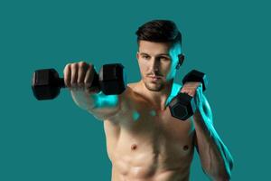 A shirtless man is shown standing on a green background while holding dumbbells in each hand. He appears focused and determined as he performs weightlifting exercises. photo