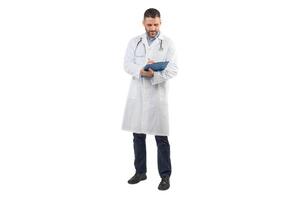 A man doctor, dressed in a white coat, stands against a white background while writing on a blue clipboard. He appears focused on his task, indicating a commitment to his medical duties. photo