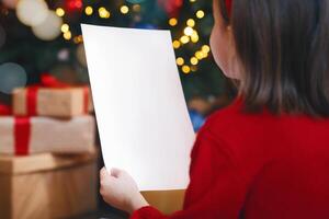 Back view of little girl holding blank white empty paper over Christmas festive background, mockup, free space photo
