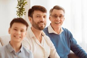 Multi-Generational Family. Joyful Senior Man, His Adult Son And Grandson Boy Smiling At Camera Sitting On Sofa At Home. photo