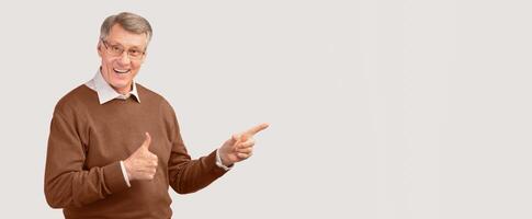 I Like It. Smiling Senior Gentleman Gesturing Thumbs Up Pointing Fingers Aside Standing On White Studio Background. Free Space, Panorama photo