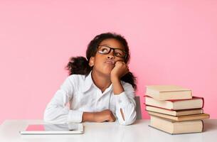 Bored Black School Girl Sitting Between Tablet Computer And Book Stack On Yellow Background In Studio. Boring Homework Concept photo