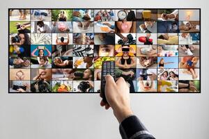 A persons hand is shown holding a remote control, pointing at a television screen. The television screen displays a collage of various images, each depicting a different activity or scene. photo