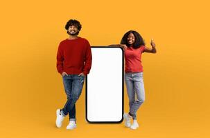 A man and a woman are standing next to a blank screen, both posing as if they are presenting something. The blank screen offers a versatile space for text or images. photo