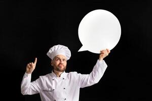 Funny Chef Man Holding Empty White Speech Bubble Pointing Finger Up Having Idea Posing Over Black Background. Studio Shot, Mockup photo