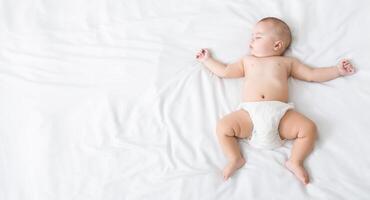 Cute newborn baby in diaper napping on white blanket with his arms up, top view, copy space photo