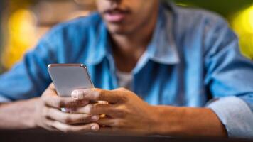 Cropped of black guy is seated at a table, engrossed in his cell phone. He is focused on the screen, tapping and scrolling. His surroundings are modern and minimalistic. photo