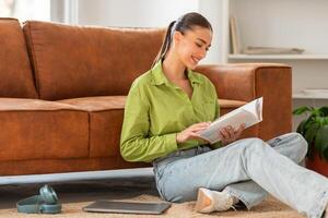 A woman is seated on the floor, engrossed in a book she is reading. The woman appears focused as she flips through the pages, immersed in the content of the book. photo