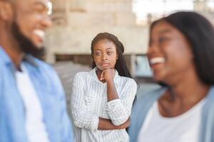 Upset black woman watching her ex boyfriend happy in relations with new girlfriend, looking jealous on background, selective focus photo