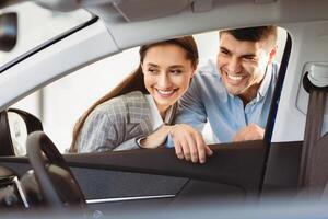 Taking A Closer Look. Beautiful smiling couple examining car before buying at the dealership, view from the inside photo