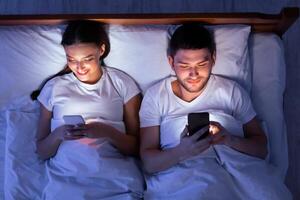 Couple Using Smartphones Ignoring Each Other Lying In Bed At Home At Night. Modern Relationship Problems. Top View photo