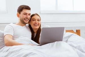 Cheerful Couple Watching Movie On Laptop Lying In Bed At Home. Family Weekend Morning. Selective Focus photo