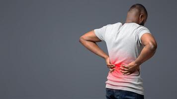Afro guy holding both hands on lower back, pain in spine, inflamed zone highlighted in red, white background, free space photo
