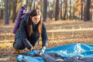 Girl backpacker setting up tent, forest background, copy space photo