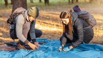 Couple of tourists pitching tent, having break in sun lights in autumn forest photo