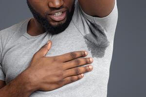 Close up of black guy disgusted by bad odor, smelling wet armpit, white background, free space photo