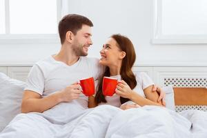 Good Morning. Happy Couple Having Coffee Hugging Lying In Bed At Home. photo