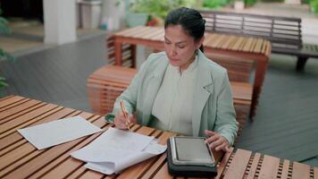 Professional businesswoman checking documents and using tablet while working outdoors, handling financial or administrative tasks under pressure, analyzing company fees, calculating expense concepts. video