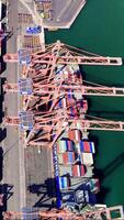 Aerial views showcase a container ship docked for cargo loading by three cranes, while nearby tugboats assist with maneuvering operations video