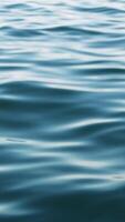 Gentle waves ripple across a deep blue body of water, reflecting the sky's hues on its surface, creating a serene and tranquil atmosphere video