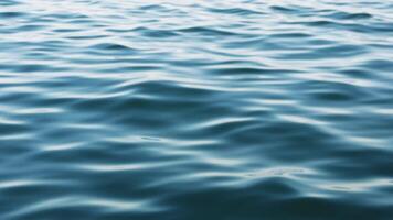Gentle waves ripple across a deep blue body of water, reflecting the sky's hues on its surface, creating a serene and tranquil atmosphere video