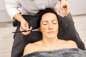 Crop cosmetologist applying facial product on face of client during beauty session photo