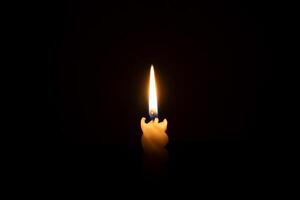 A single burning candle flame or light glowing on a spiral white candle on black or dark background on table in church for Christmas, funeral or memorial service with copy space photo