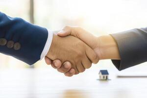 Two business people shaking hands over a table with a house photo
