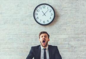 Tired Businessman Yawning in Front of Clock on Brick Wall photo