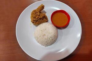 Crispy chicken, chili sauce and white rice on a white plate on the dining table photo