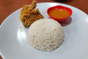 Crispy chicken, chili sauce and white rice on a white plate on the dining table photo