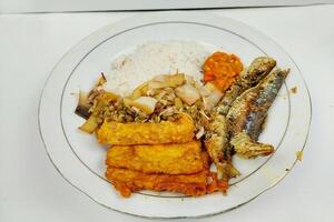 Rice mixed with fried fish and tempeh vegetables on a white plate, on the table photo