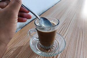 Coffee milk is stirred in a glass using a spoon on the table photo