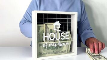 a idosos mulher lugares dólar contas para dentro uma decorativo poupança caixa etiquetado para dela Sonhe casa, ilustrando dela comprometimento para financeiro planejamento e casa propriedade video