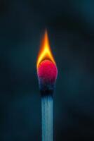 A close-up of a lit matchstick creating a vibrant flame against a dark background photo