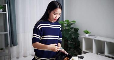 Handheld high angle view shot, Young Asian woman is scooping food out of plastic container into bowls to prepare for lunch on the table at home. Home lifestyle. video