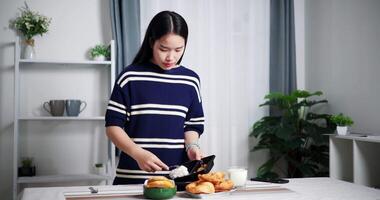 Handheld shot, Young Asian woman pouring food from plastic container into bowl ready for lunch on table at home. Lifestyle at home video