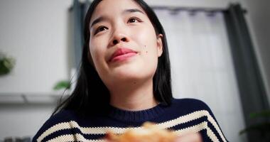 Handheld selective focus shot, Happy Asian woman eating a hamburger in the morning at table in living room. Home Lifestyle. Eating and drinking concept. video