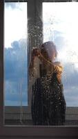 A child is standing in front of a window with water dripping down video