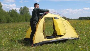a man assembles and sets up a yellow tent while camping in a wild field video