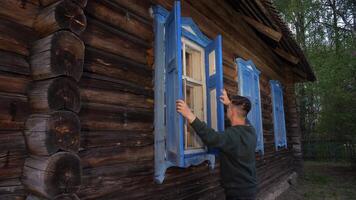 a man opens the shutters on a window in an old wooden house. video