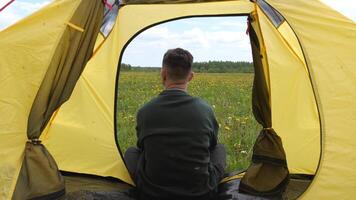 a man sitting in a tent enjoying the view of the field and forest, wildlife video