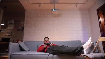 gamer man lying on sofa and playing games on console using controller video